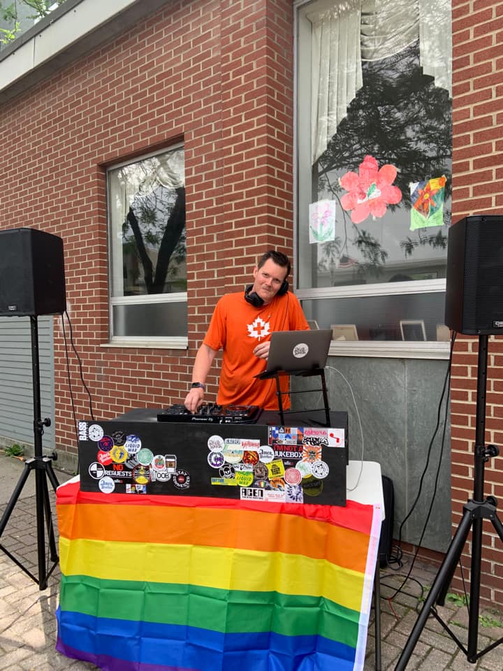 A person stands in downtown Bennington operating a DJ booth. The booth is covered with a pride flag.
