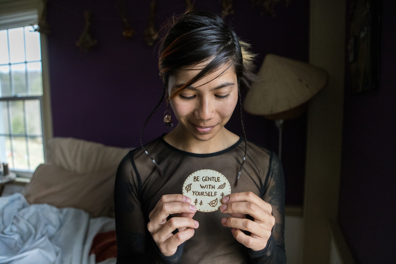 A person with black hair and brown skin holds a circular card which reads 'be gentle with yourself.'